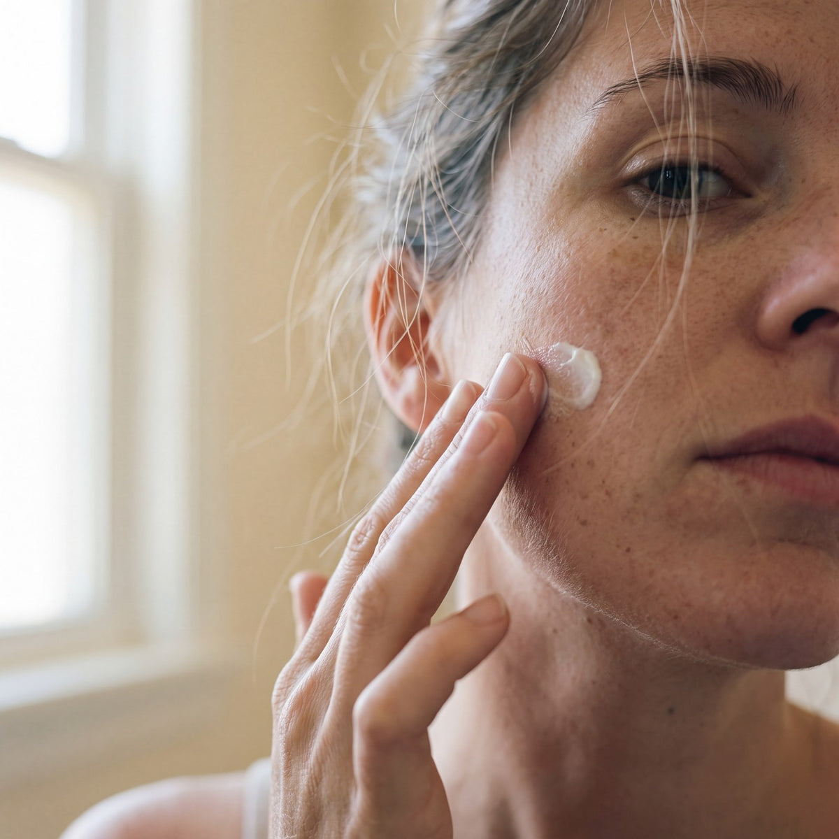 Mujer aplicandose crema facial en la mejilla