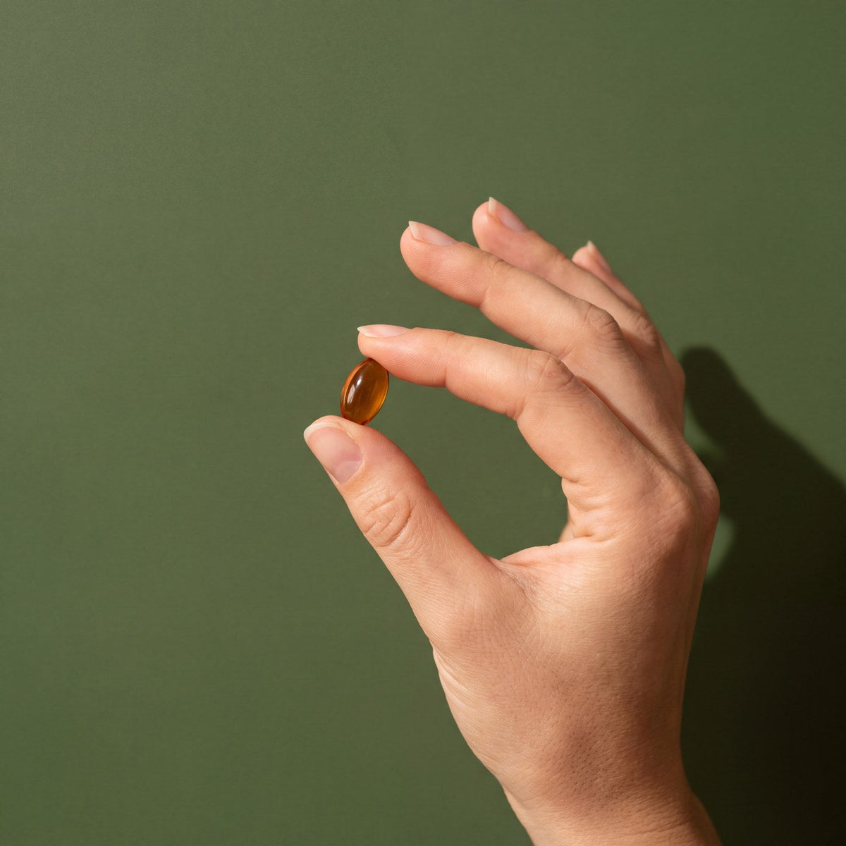 Mano sosteniendo una capsula sobre fondo verde oliva